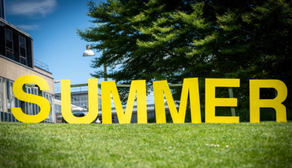 Large yellow capital letters spelling the word 'summer' located on campus by the lake as part of the Summer at Bath programme.
