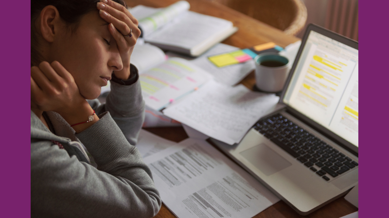 Woman sits at desk with laptop, looking tired