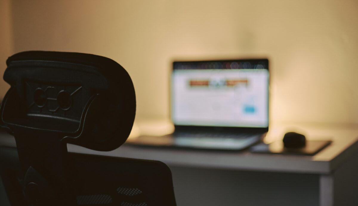 A laptop on a desk with an empty chair in front