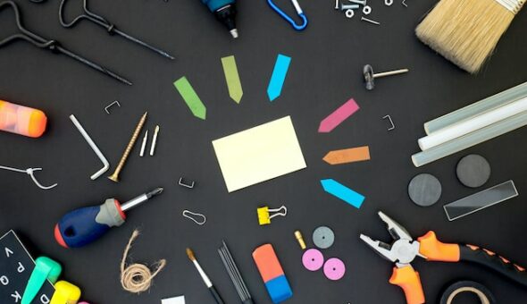 An assortment of tools and accessories arranged on a table and photographed top down, including Post-It notes, a screwdriver and pliers.