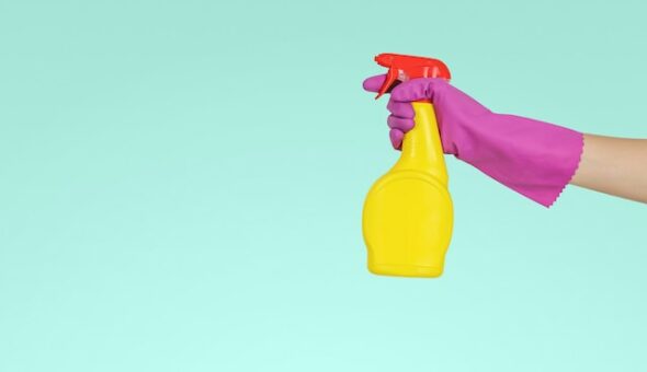 An extended arm in a pink rubber glove holds a yellow cleaning spray bottle.