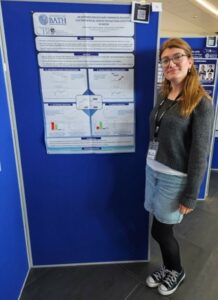 Meltem Agar smiles to camera stood next to board displaying their poster