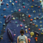 Woman facing up at a tall climbing wall with multiple routes to climb up it