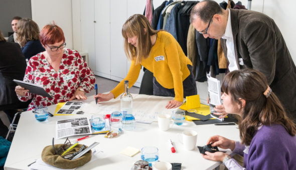 Four people stand around a table and take part in a sorting activity to work out shared aims for a collaborative project