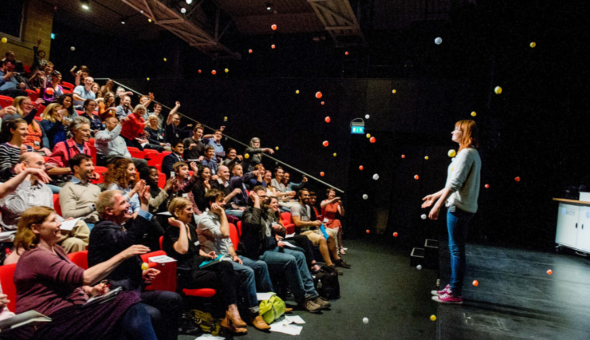 A woman standing in front of a large crowd sat on tiered seating.