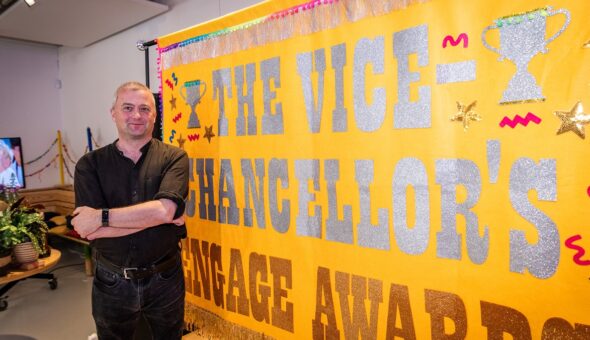 A white man stands in front of a large banner that says the words 'Vice-Chancellor's Engage Awards'